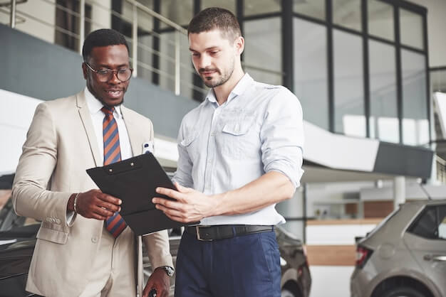 Free photo a young black businesswoman signs documents and buys a new car. the car dealer is standing next to him.