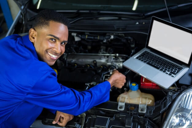 Free photo mechanic examining car engine with help of laptop