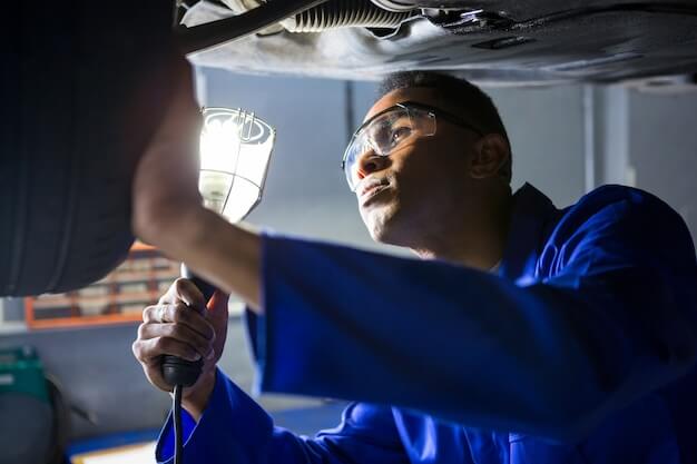 Free photo mechanic examining car tyre using flashlight