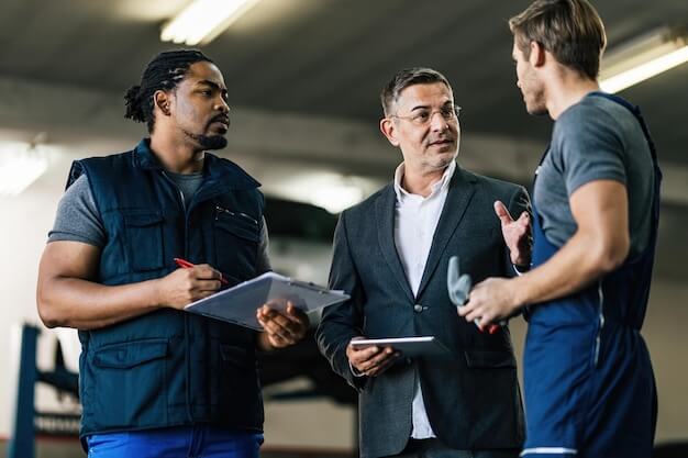 Free photo mid adult manager using digital tablet while talking to car mechanics in auto repair shop