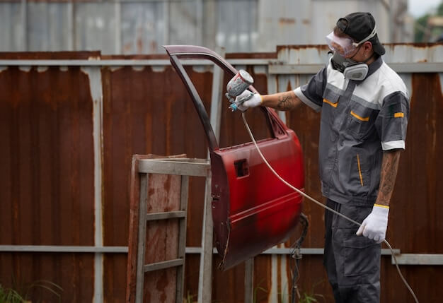 Man spraying powder paint on car door medium shot