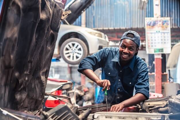 Photo african maintenance male checking tire service via insurance system at garage with smile and happy