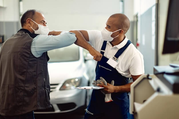 Photo happy mechanic and his foreman greeting with elbows in repair shop during covid19 pandemic