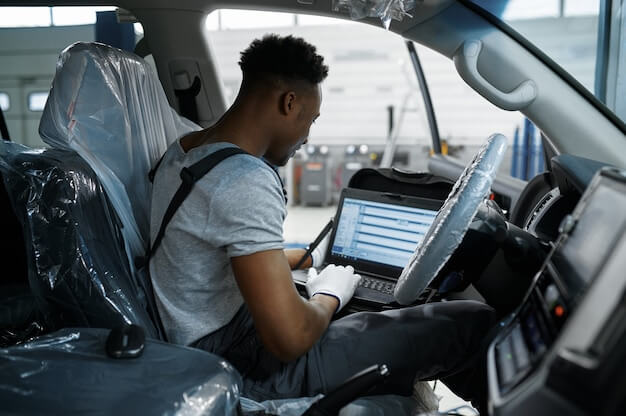 Photo mechanic man using laptop at the auto with opened hood in mechanical workshop