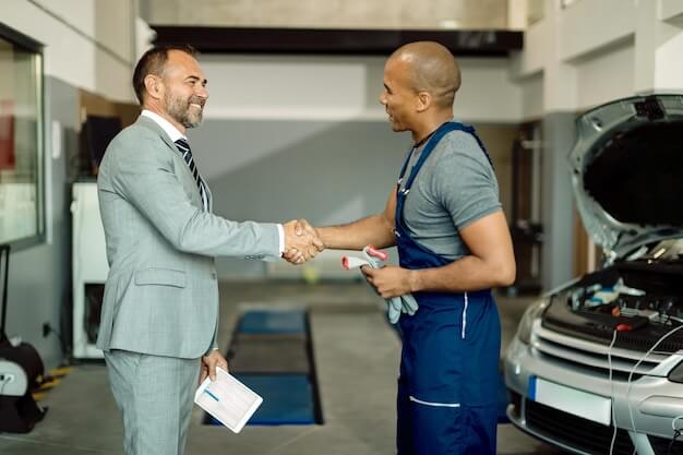 Free photo happy businessman and african american mechanic handshaking at auto repair shop