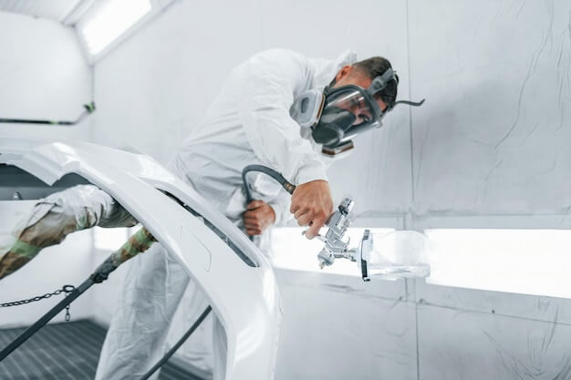 Photo in protective mask painting the car caucasian automobile repairman in uniform works in garage