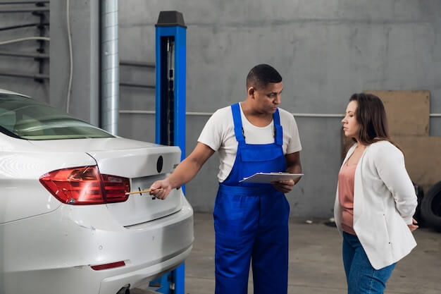 Photo mechanic with clipboard discusses car repair with woman